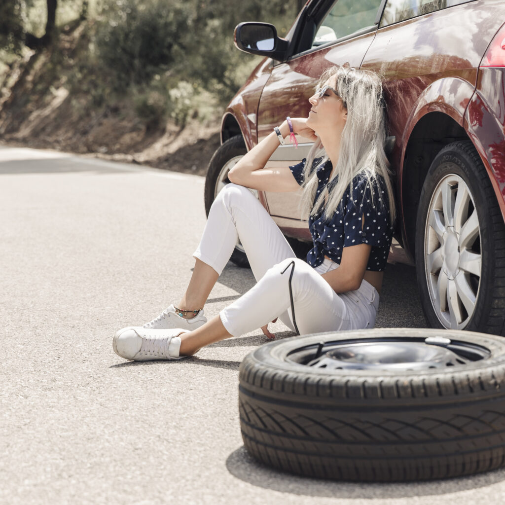 woman sitting along side a car with a flat tire